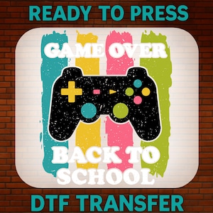 May include: A DTF transfer featuring a black video game controller graphic centered over vertical brush strokes in teal, yellow, pink, and lime green. The white text reads READY TO PRESS, GAME OVER, BACK TO SCHOOL, and DTF TRANSFER.