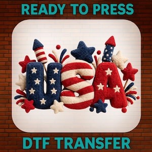May include: A DTF transfer design spelling "USA" in red, white, and blue, with star and firework accents. The design is set against a white background with the text "READY TO PRESS" and "DTF TRANSFER".