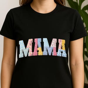 Puede incluir: Camiseta negra con la palabra "MAMA" en letras grandes y coloridas de patchwork. Las letras est&aacute;n decoradas con estampados florales y de cuadros en tonos azules, rosas, amarillos y blancos. La camiseta tiene mangas cortas y cuello redondo.