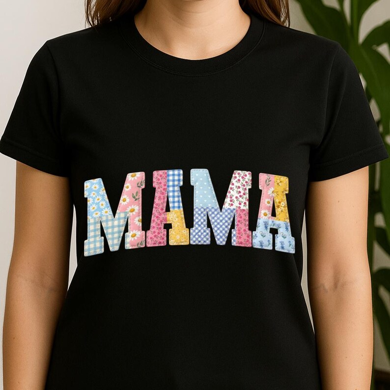 Puede incluir: Camiseta negra con la palabra "MAMA" en letras grandes y coloridas de patchwork. Las letras est&aacute;n decoradas con estampados florales y de cuadros en tonos azules, rosas, amarillos y blancos. La camiseta tiene mangas cortas y cuello redondo.