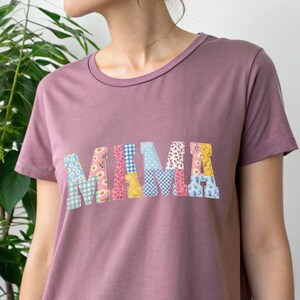 Puede incluir: Camiseta de color malva con la palabra "MAMA" aplicada en el pecho. Las letras est&aacute;n hechas de varias telas florales y estampadas en tonos de azul, rosa, amarillo y blanco. La camiseta tiene cuello redondo y mangas cortas.
