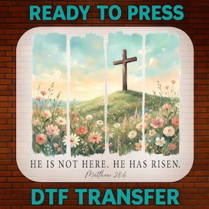 Peut inclure: Motif de transfert DTF avec un paysage à l'aquarelle représentant une croix en bois sur une colline, entourée de fleurs colorées. Le texte "READY TO PRESS" et "DTF TRANSFER" sont en haut et en bas, avec la citation "HE IS NOT HERE. HE HAS RISEN. Matthew 28:6" au centre.