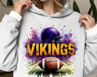 May include: A light gray hoodie featuring a purple football helmet, a brown football, and the word "VIKINGS" in gold letters. The design includes colorful paint splatters and a green field.