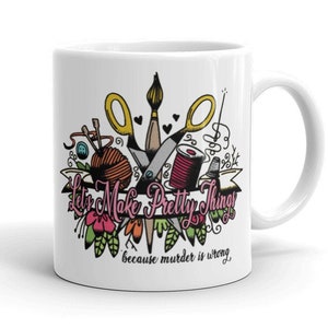 May include: White ceramic mug with a colorful illustration of sewing and crafting tools, including scissors, thread, needles, and a paintbrush. The text "Let's Make Pretty Things because murder is wrong" is printed on the mug.