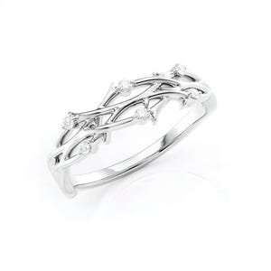 Puede incluir: Un anillo de plata con un delicado dise&ntilde;o de ramas entrelazadas. El anillo presenta peque&ntilde;as piedras preciosas redondas y claras engastadas a lo largo de las ramas. El anillo est&aacute; sobre un fondo blanco, resaltando sus intrincados detalles.