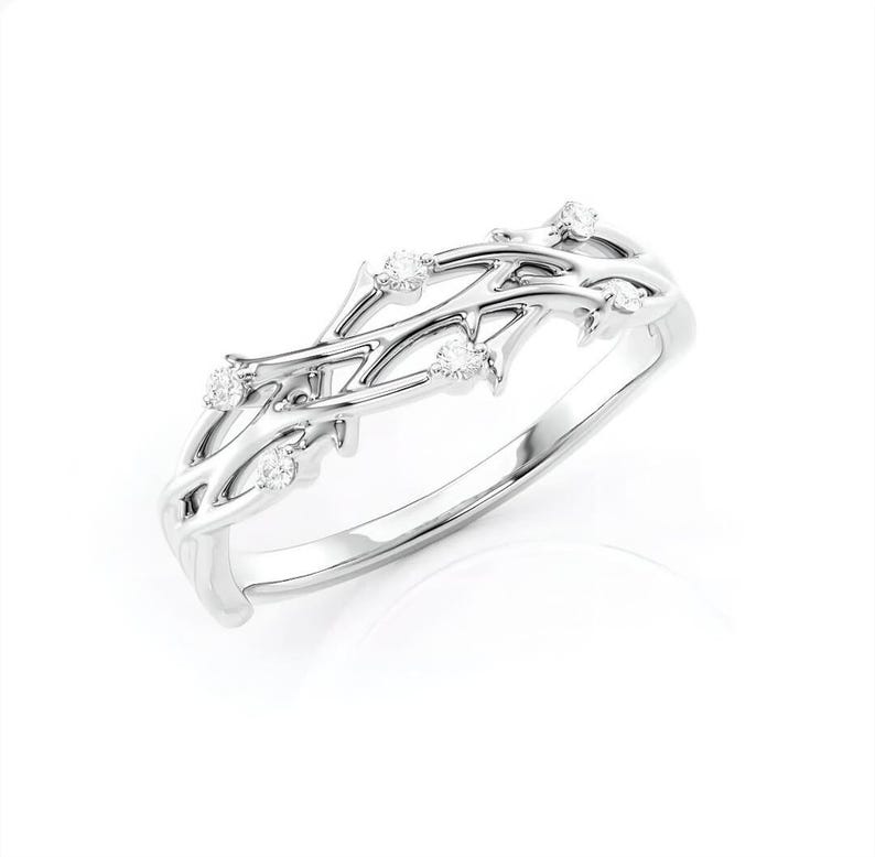 Puede incluir: Un anillo de plata con un delicado dise&ntilde;o de ramas entrelazadas. El anillo presenta peque&ntilde;as piedras preciosas redondas y claras engastadas a lo largo de las ramas. El anillo est&aacute; sobre un fondo blanco, resaltando sus intrincados detalles.