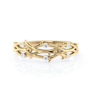 Puede incluir: Un anillo dorado con un delicado dise&ntilde;o de vid. El anillo presenta peque&ntilde;as piedras preciosas redondas y claras, colocadas a intervalos a lo largo de la vid. El anillo se muestra sobre un fondo blanco.