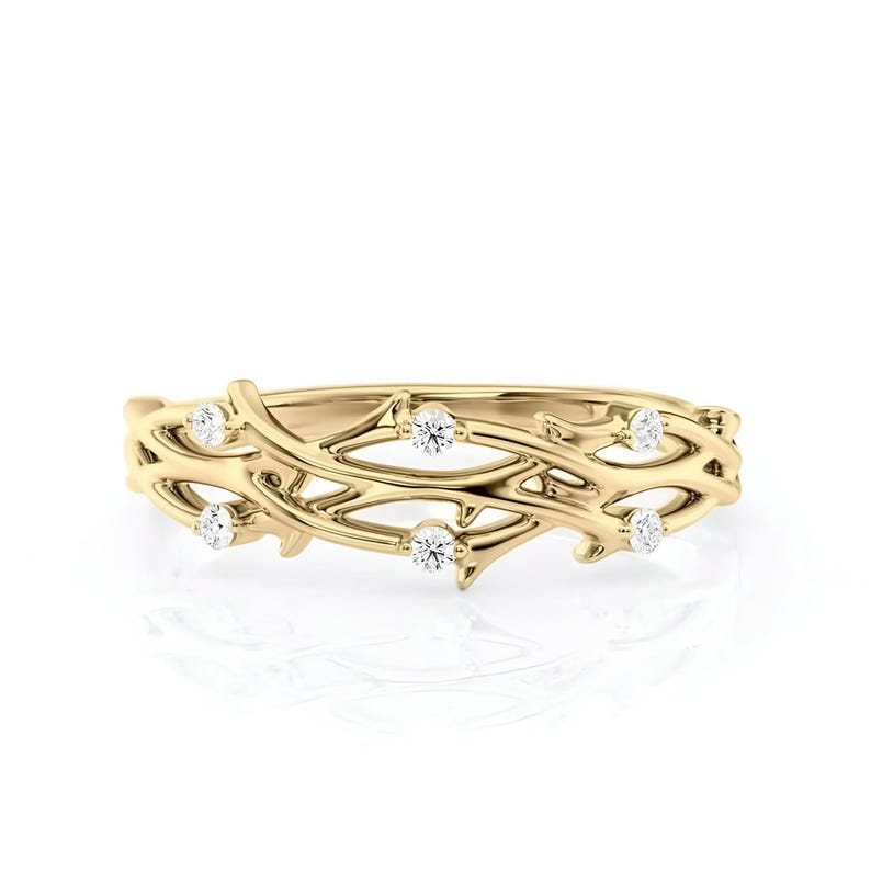 Puede incluir: Un anillo dorado con un delicado dise&ntilde;o de vid. El anillo presenta peque&ntilde;as piedras preciosas redondas y claras, colocadas a intervalos a lo largo de la vid. El anillo se muestra sobre un fondo blanco.