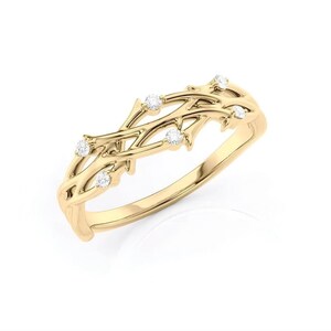 Puede incluir: Un anillo dorado con un delicado dise&ntilde;o de ramas entrelazadas. El anillo presenta peque&ntilde;as piedras preciosas redondas y transparentes engastadas a lo largo de las ramas. Es una joya.