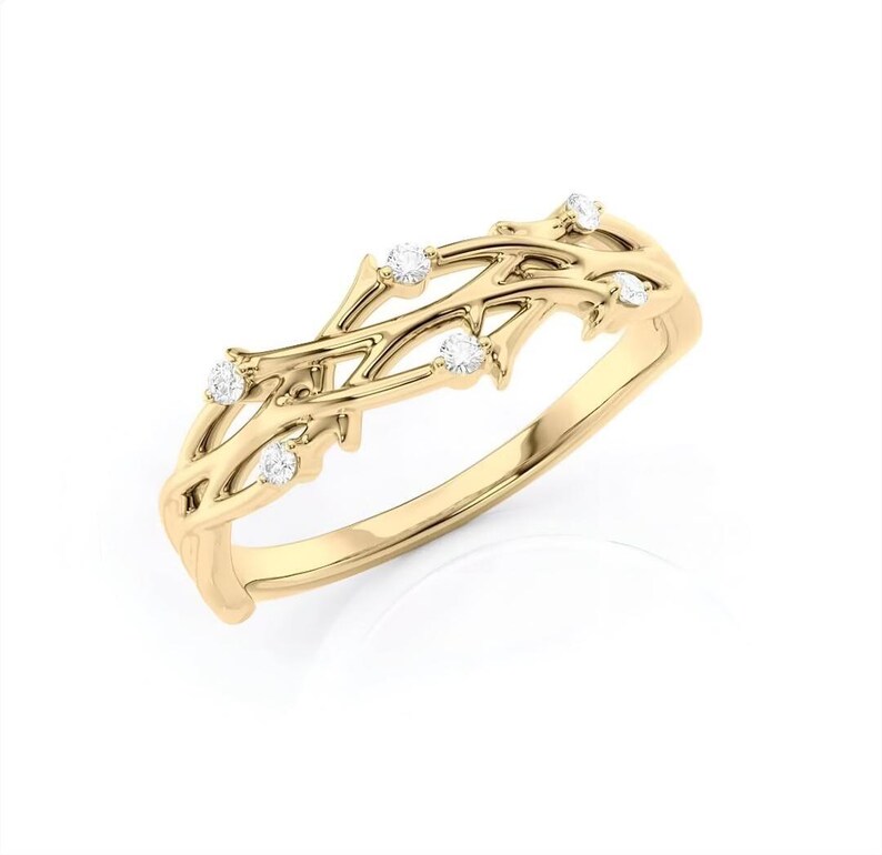 Puede incluir: Un anillo dorado con un delicado dise&ntilde;o de ramas entrelazadas. El anillo presenta peque&ntilde;as piedras preciosas redondas y transparentes engastadas a lo largo de las ramas. Es una joya.
