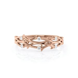 Puede incluir: Un anillo de oro rosa con un delicado dise&ntilde;o de vid entrelazada. El anillo presenta seis peque&ntilde;as piedras preciosas redondas y claras, espaciadas uniformemente a lo largo de la vid. El anillo est&aacute; sobre un fondo blanco.