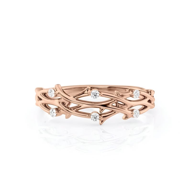 Puede incluir: Un anillo de oro rosa con un delicado dise&ntilde;o de vid entrelazada. El anillo presenta seis peque&ntilde;as piedras preciosas redondas y claras, espaciadas uniformemente a lo largo de la vid. El anillo est&aacute; sobre un fondo blanco.