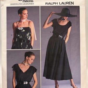 May include: A white ceramic mug with a black handle and the text "But first, coffee" in a handwritten style. The mug is on a white surface. The mug is approximately 10 cm tall.