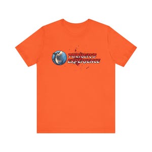 May include: Bright orange t-shirt featuring a cartoon shark with a blue and white design inside a circle. The text "Tucker's Experience" is printed in red and white, with red splatter accents.