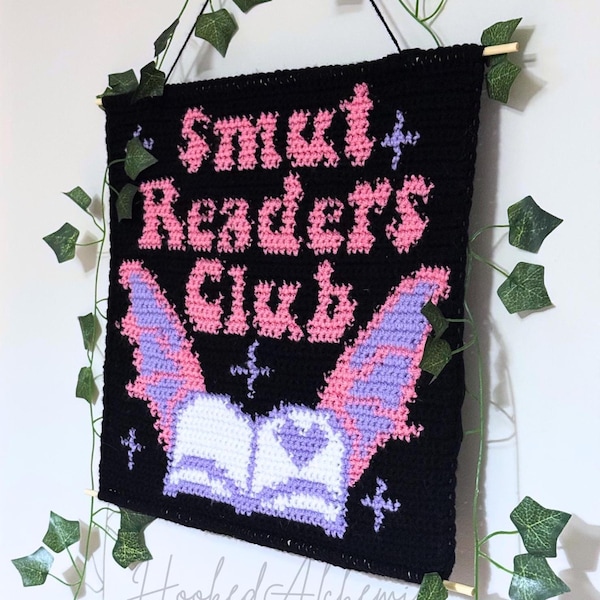 Peut inclure: Suspension murale en crochet noir avec le texte "Smut Readers Club" en rose. En dessous, une chauve-souris aux ailes roses et violettes au-dessus d'un livre ouvert. Décoré de fausse vigne.