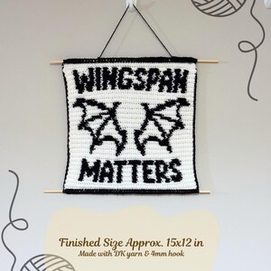 K&ouml;nnte beinhalten: Geh&auml;keltes Wandbild mit dem Text "WINGSPAN MATTERS" in Schwarz auf Wei&szlig;, mit fledermausartigen Fl&uuml;geln. Fertige Gr&ouml;&szlig;e ca. 38x30 cm. Aufgeh&auml;ngt mit schwarzem Faden und Holzst&auml;ben, ein einzigartiges Wohnaccessoire.