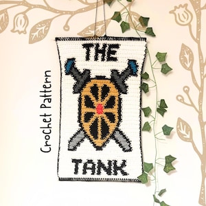 May include: A white crochet banner with the words "THE TANK" in black block letters. The banner features a shield design with crossed swords and a wheel. The words "Crochet Pattern" are written vertically on the left side.