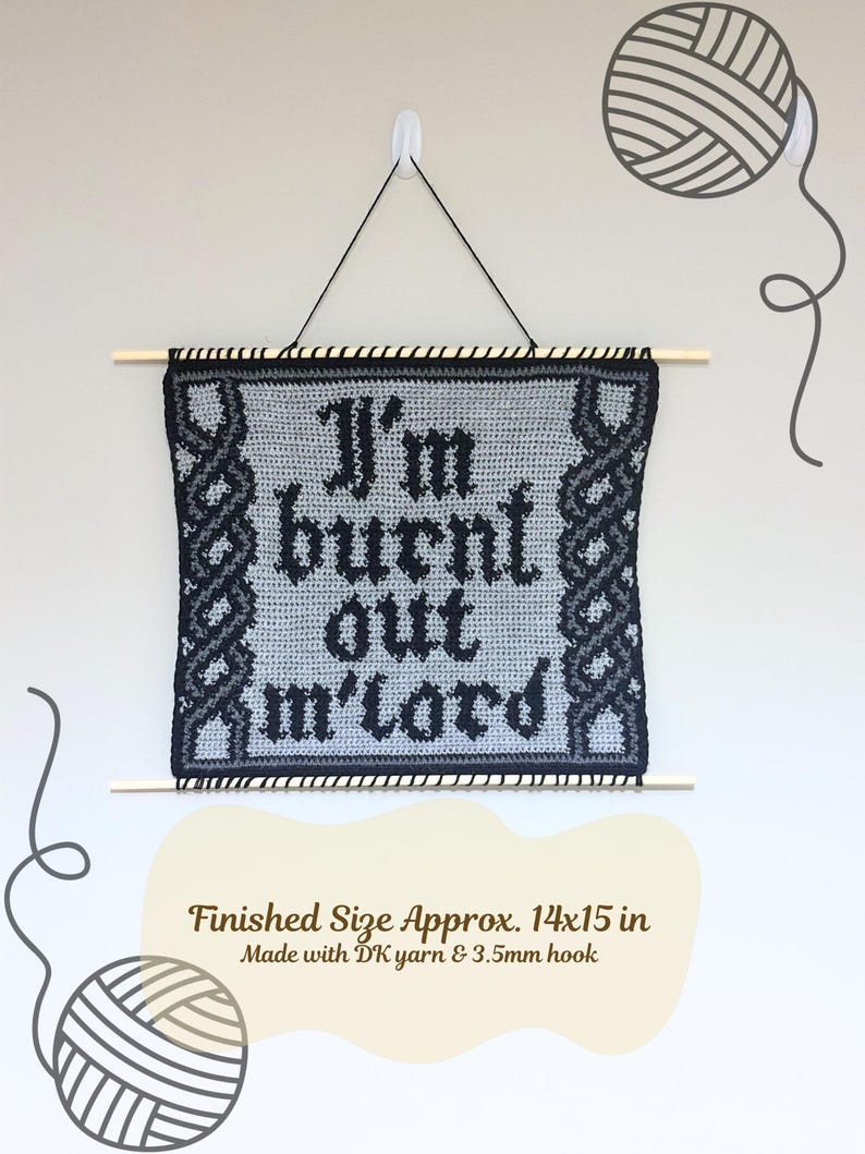 Op de afbeelding: Een handgemaakte, grijs en zwart gehaakte wandhanger met de tekst "I'm burnt out m'lord". De afmeting is ongeveer 35,5 x 38 cm. Opgeschort aan een houten stok met zwart touw.