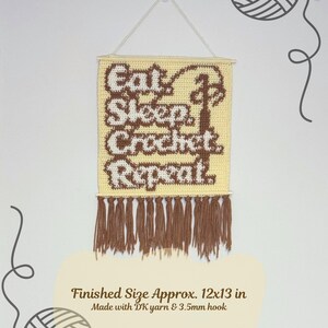 May include: A crocheted wall hanging with the words "Eat, Sleep, Crochet, Repeat" in brown and white. The finished size is approximately 12x13 inches. It has a fringe at the bottom and is suspended by a string.