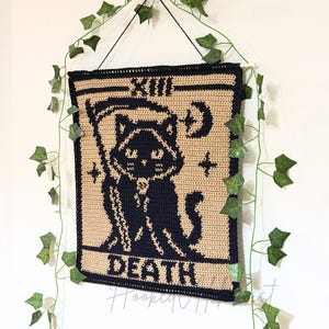 May include: A rectangular crochet wall hanging featuring a black cat dressed as the Grim Reaper with a scythe. The design includes the Roman numeral XIII at the top and the word DEATH at the bottom, rendered in black yarn against a tan background.