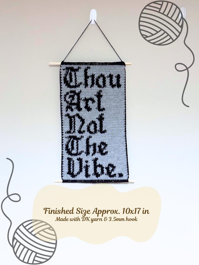 Op de afbeelding: Een handgemaakte, lichtgrijze gehaakte wandhanger met de tekst "Thou Art Not The Vibe" in zwarte gotische letters. De afmeting is ongeveer 25 x 43 cm. Het is opgehangen aan een houten stok met zwart touw.
