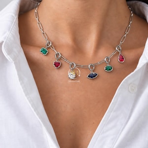 May include: A silver-toned paperclip chain necklace featuring six dangling charms with multi-colored gemstones, including emerald green, ruby red, sapphire blue, and a clear round stone. The text SilverGold is printed near the center charm.