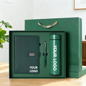 Può includere: Un set regalo verde scuro composto da un taccuino, una penna e una bottiglia d'acqua. Il taccuino ha una chiusura argentata e il testo "YOUR LOGO". La bottiglia d'acqua ha il testo "YOUR LOGO" in bianco. Il set è in una scatola e un sacchetto regalo verdi.