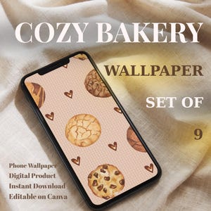 Op de afbeelding: Een smartphone toont een wallpaper met aquarelkoekjes en hartjes op een roze achtergrond. De telefoon staat tegen een neutrale stoffen achtergrond. Tekst op de telefoon luidt "COZY BAKERY WALLPAPER SET OF 9". Extra tekst geeft aan dat het een telefoon wallpaper, digitaal product, direct downloadbaar en bewerkbaar op Canva is.