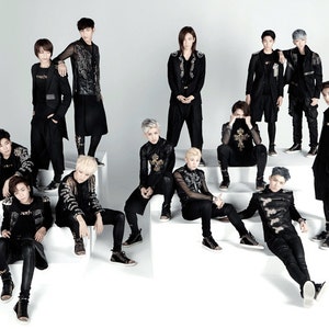May include: A group of 13 men in black clothing with gold accents pose for a photo. They are standing and sitting on a set of white steps. Some of the men are wearing jackets, while others are wearing long-sleeved shirts. All of the men are wearing black pants.