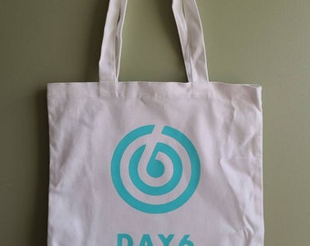 May include: White canvas tote bag with a turquoise circle logo and the text "DAY6" printed on the front.