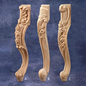 以下が含まれることがあります： 装飾的な花柄とスクロールの彫刻が施された、未完成の木製家具の脚が3つ。各脚は異なるデザインで、曲線と詳細なレリーフ加工が施されています。脚にはA、B、Cのラベルが付いています。