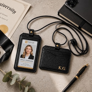 Może przedstawiać: Dwa czarne etui na identyfikatory z ziarnistej skóry z czarnymi smyczami. Pionowe etui zawiera kartę identyfikacyjną Emily Johnson z firmy Novus Solutions. Poziome etui posiada złote, wytłoczone inicjały K.G. na przedniej powierzchni.