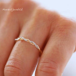 May include: A thin gold ring featuring a twisted band design with small embedded clear stones along the surface. The ring has a delicate, intertwined metal structure that creates a continuous rope-like appearance around the finger.