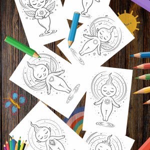Puede incluir: Varias páginas para colorear en blanco y negro que representan figuras de hadas con alas y símbolos. Las páginas están dispuestas sobre una superficie de madera, junto con lápices de colores, lo que sugiere una actividad creativa. Las ilustraciones presentan personajes con los ojos cerrados.