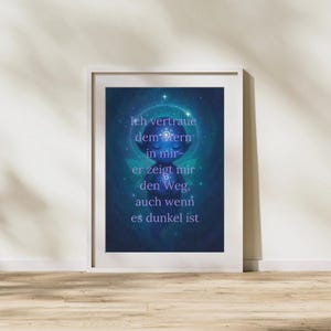 Pode incluir: Impressão artística emoldurada com um design celestial em tons de azul e roxo. A obra apresenta uma figura central com os olhos fechados, rodeada por um desenho circular e texto em alemão. A moldura é branca.