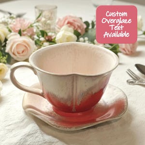 May include: A ceramic teacup and saucer set with a white and red glaze. The teacup has a handle and a scalloped rim. The saucer is a matching shape. The image includes the text "Custom Overglaze Text Available".