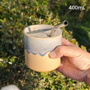 May include: A cylindrical ceramic cup with a 400mL capacity, featuring a two-tone glaze with a light beige base and a speckled grey top section separated by a wavy line. A metallic straw is inserted into the top opening of the cup.