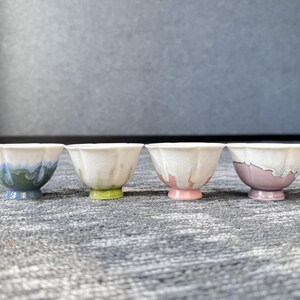 Pode incluir: Quatro pequenas tigelas de cer&acirc;mica decorativas com uma borda ondulada. Cada tigela tem uma base e uma borda de cores diferentes, incluindo azul, verde, rosa e roxo. As tigelas est&atilde;o dispostas em uma fileira em uma superf&iacute;cie texturizada.