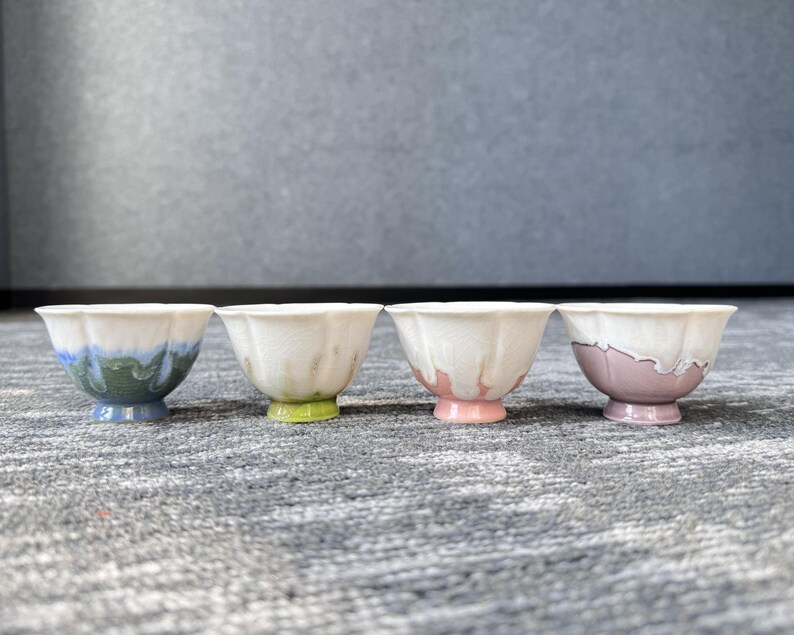 Pode incluir: Quatro pequenas tigelas de cer&acirc;mica decorativas com uma borda ondulada. Cada tigela tem uma base e uma borda de cores diferentes, incluindo azul, verde, rosa e roxo. As tigelas est&atilde;o dispostas em uma fileira em uma superf&iacute;cie texturizada.