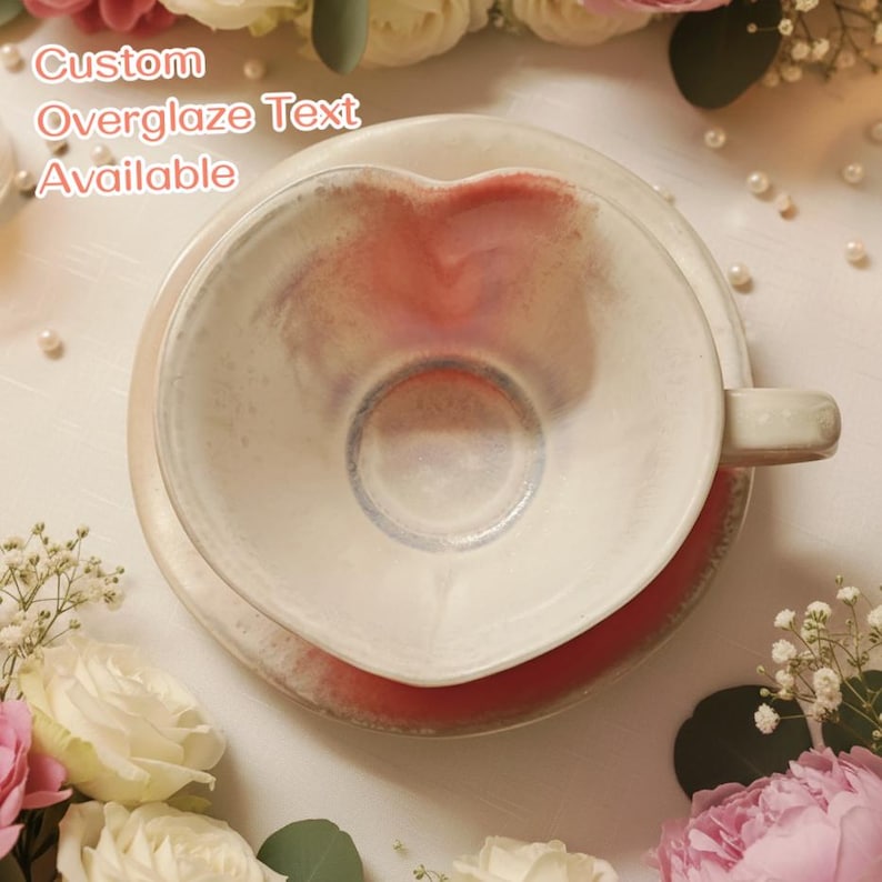 May include: A heart-shaped ceramic teacup and saucer set. The cup and saucer are white with a red and pink interior. The text "Custom Overglaze Text Available" is visible in the image.