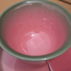 Puede incluir: Un cuenco de cer&aacute;mica con interior rosa vibrante y borde verde claro, que presenta un acabado de esmalte craquelado en toda la superficie. El cuenco se acompa&ntilde;a de un plato a juego que muestra el mismo tono rosa y textura craquelada.