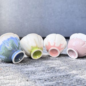 Pode incluir: Quatro pequenas tigelas de cer&acirc;mica com um design &uacute;nico em forma de p&eacute;tala. As tigelas apresentam uma variedade de cores, incluindo azul, branco, rosa e verde. Cada tigela tem uma cor diferente por dentro e por fora, com uma cor contrastante na base.