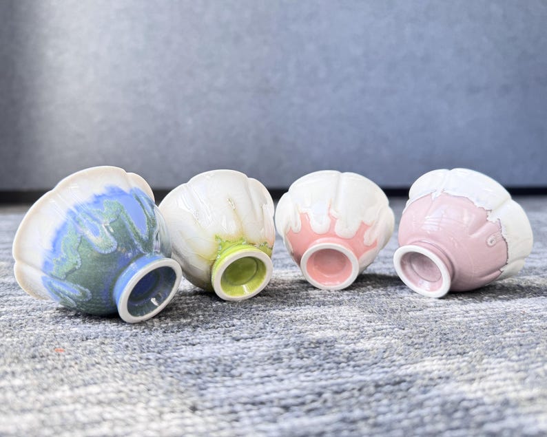 Pode incluir: Quatro pequenas tigelas de cer&acirc;mica com um design &uacute;nico em forma de p&eacute;tala. As tigelas apresentam uma variedade de cores, incluindo azul, branco, rosa e verde. Cada tigela tem uma cor diferente por dentro e por fora, com uma cor contrastante na base.