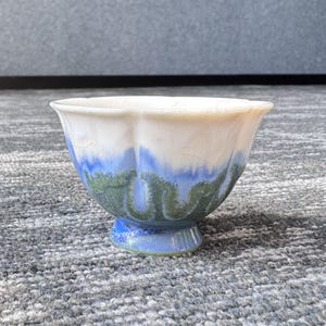Pode incluir: Uma tigela de cer&acirc;mica com base de pedestal. A tigela apresenta um interior e borda brancos, que transitam para tons azuis e verdes no exterior. A cobertura tem um efeito craquelado, adicionando textura. A tigela &eacute; provavelmente feita &agrave; m&atilde;o.