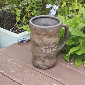 Puede incluir: Una taza de cer&aacute;mica marr&oacute;n con una superficie texturizada similar a la corteza y un interior oscuro. La taza cuenta con un asa en el lado derecho y texto impreso en blanco que dice: Michael- Morning Person (After Coffee). Forma cil&iacute;ndrica.