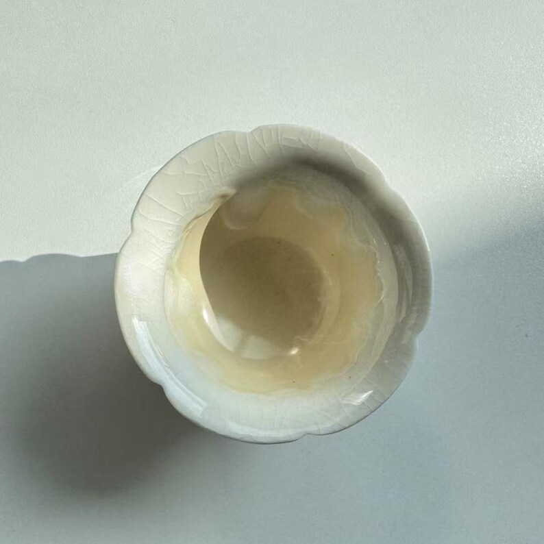 Pode incluir: Uma pequena tigela de cer&acirc;mica esbranqui&ccedil;ada com borda ondulada. O interior tem um tom amarelo p&aacute;lido e o exterior mostra um efeito de esmalte rachado. A tigela &eacute; provavelmente feita &agrave; m&atilde;o e adequada para servir pequenas por&ccedil;&otilde;es.