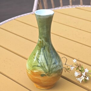K&ouml;nnte beinhalten: Eine handbemalte Keramikvase mit schlankem Hals und bauchigem K&ouml;rper. Die Vase hat einen Farbverlauf, der von einem warmen orangefarbenen Sockel zu einem gr&uuml;nen oberen Bereich mit floralen Akzenten &uuml;bergeht. Der Innenraum ist hellblau.