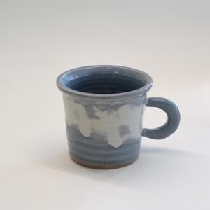 May include: A ceramic mug with a rounded handle. The mug has a blue and white glaze, with a darker blue interior. The mug has a rustic, textured appearance. Ideal for tea or coffee, it's a charming addition to any kitchen.