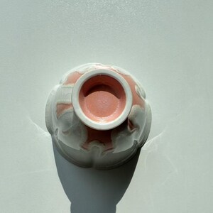 Pode incluir: Uma tigela de cer&acirc;mica com exterior branco e interior rosa. A tigela tem um design floral e &eacute; vista de baixo, mostrando o interior rosa e a borda branca.