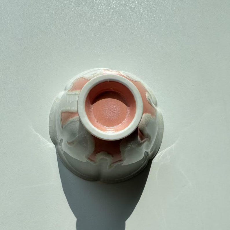 Pode incluir: Uma tigela de cer&acirc;mica com exterior branco e interior rosa. A tigela tem um design floral e &eacute; vista de baixo, mostrando o interior rosa e a borda branca.
